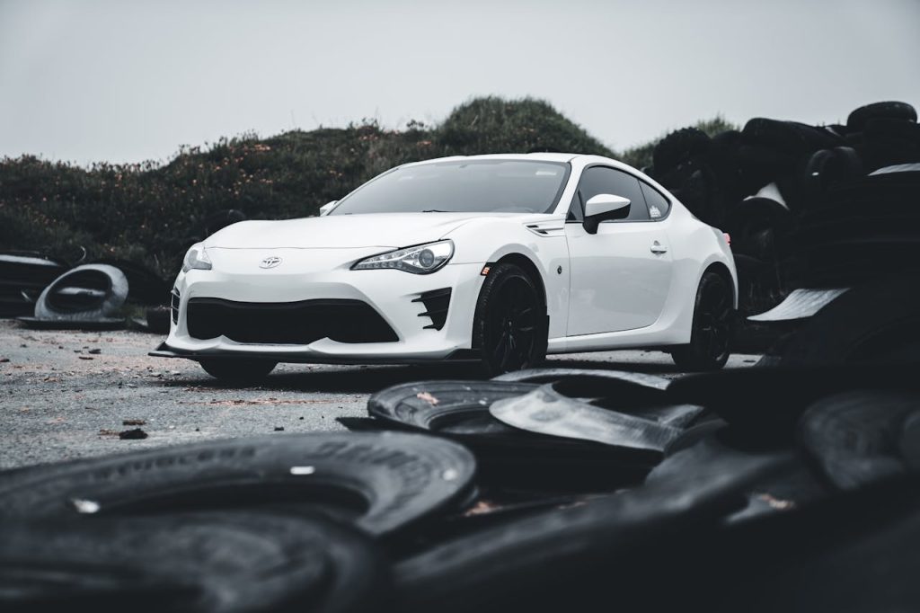 A modern white sports car parked in an outdoor location, surrounded by old tires.